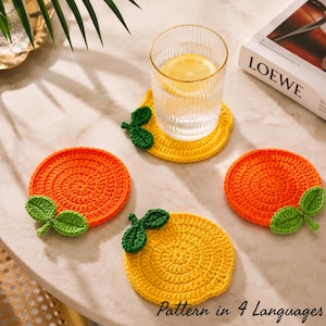 May include: Four handmade crochet coasters in the shape of citrus fruits. Two are orange, and two are yellow, each with green leaf accents. A glass of water with a lemon slice sits on one coaster. The text "Pattern in 4 Languages" is at the bottom.