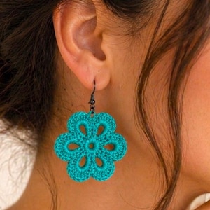Op de afbeelding: Turquoise gehaakte bloemen oorbellen. De oorbellen zijn fel turquoise van kleur en hebben een gedetailleerd bloemendesign. De tekst "Pattern in 4 Languages" is ook zichtbaar.