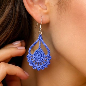 May include: A pair of blue crochet teardrop earrings with a floral design. The earrings are suspended from silver-coloured hooks. The image includes the text "Pattern in 4 Languages".