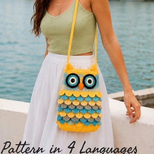 May include: A crochet owl-shaped crossbody bag featuring a yellow, blue, and grey layered feather pattern. The bag has large circular eyes with black pupils, a small orange beak, and a long yellow shoulder strap, crafted with textured yarn.
