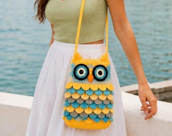May include: A crochet owl-shaped crossbody bag featuring a yellow, blue, and grey layered feather pattern. The bag has large circular eyes with black pupils, a small orange beak, and a long yellow shoulder strap, crafted with textured yarn.
