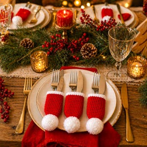 Peut inclure: Une table de No&euml;l festive avec des couverts dans des &eacute;tuis tricot&eacute;s rouges et blancs en forme de chapeaux de P&egrave;re No&euml;l. La table est d&eacute;cor&eacute;e de bougies, de verdure et de baies, cr&eacute;ant une ambiance chaleureuse.
