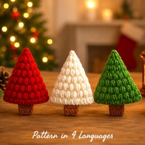 Può includere: Tre piccoli alberi decorativi a forma di cono realizzati in filato con un motivo a punti testurizzati. Gli alberi sono rossi, bianchi e verdi, ognuno dotato di una piccola base rettangolare marrone. Il testo "Pattern in 4 Languages" è visibile in basso.