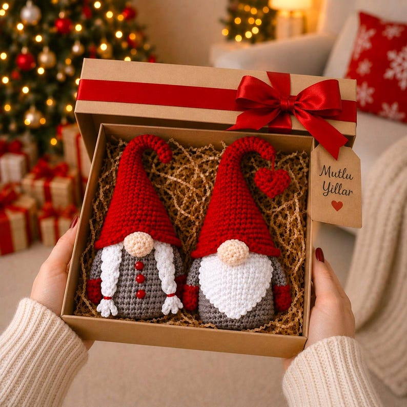 Peut inclure: Un coffret cadeau avec un ruban rouge contient deux gnomes crochet&eacute;s. L'un a une barbe blanche, l'autre des tresses blanches. Les deux ont des chapeaux rouges et des corps gris. La bo&icirc;te porte l'inscription "Mutlu Yillar".