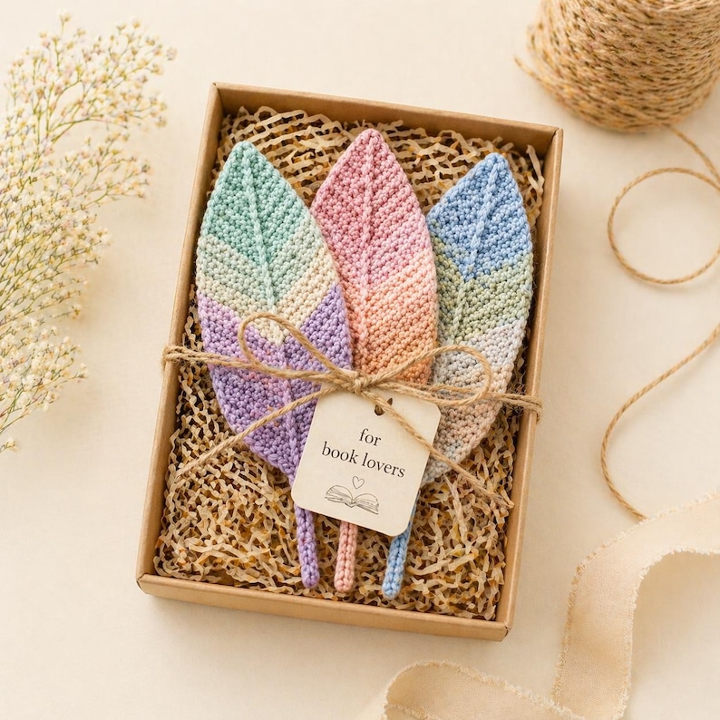 May include: A set of three crocheted feather bookmarks in a gift box. The feathers are pastel colors: green, pink, and blue. A tag tied with twine reads "for book lovers" with a small heart and book illustration.