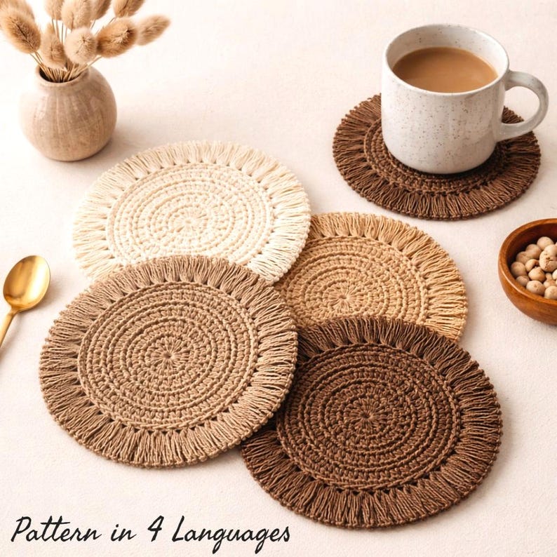 Set of four handmade crochet coasters in neutral coffee tones including cream, beige, tan and brown, arranged on a soft light background. One coaster is styled with a coffee mug on top, creating a cozy boho home aesthetic. Perfect for rustic decor, coffee lovers and handmade gift ideas. Crochet coaster PDF pattern available in 4 languages: English, German, French and Spanish.