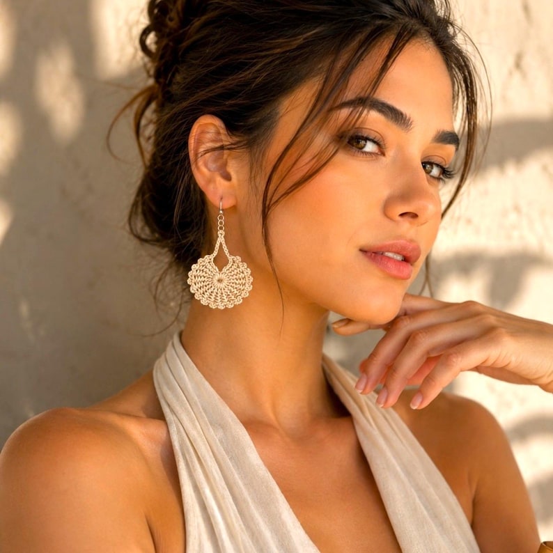May include: A pair of beige crochet earrings. The earrings have a circular design with a detailed, open weave pattern. The earrings are suspended from a delicate silver-colored hook.