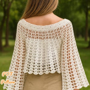 May include: Cream-colored crochet top with a wide neckline and bell sleeves. The top features an open, lacy pattern and a scalloped hemline. The text "PDF Pattern" is visible in the lower left corner. The top is made of a soft, lightweight yarn.