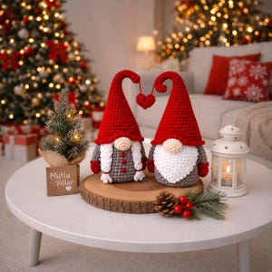 Peut inclure: Deux gnomes en crochet avec des chapeaux rouges et des tenues grises, reli&eacute;s par un ornement en forme de c&oelig;ur. Ils sont pos&eacute;s sur une tranche de bois, avec un petit sapin de No&euml;l et une lanterne. Le texte sur le panneau en bois dit "Mutlu Yillar".