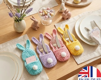 May include: A table setting with four colorful, crocheted bunny-shaped utensil holders in blue, purple, pink, and yellow. Each holder contains a fork and knife. Easter-themed decorations include ceramic bunnies and pastel-colored candies.