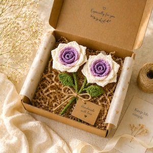 May include: Two handmade crochet roses in a gift box. The roses have white petals with purple centers and green leaves. The box is brown with the text "Especially for you" and a tag that says "Handmade with love".