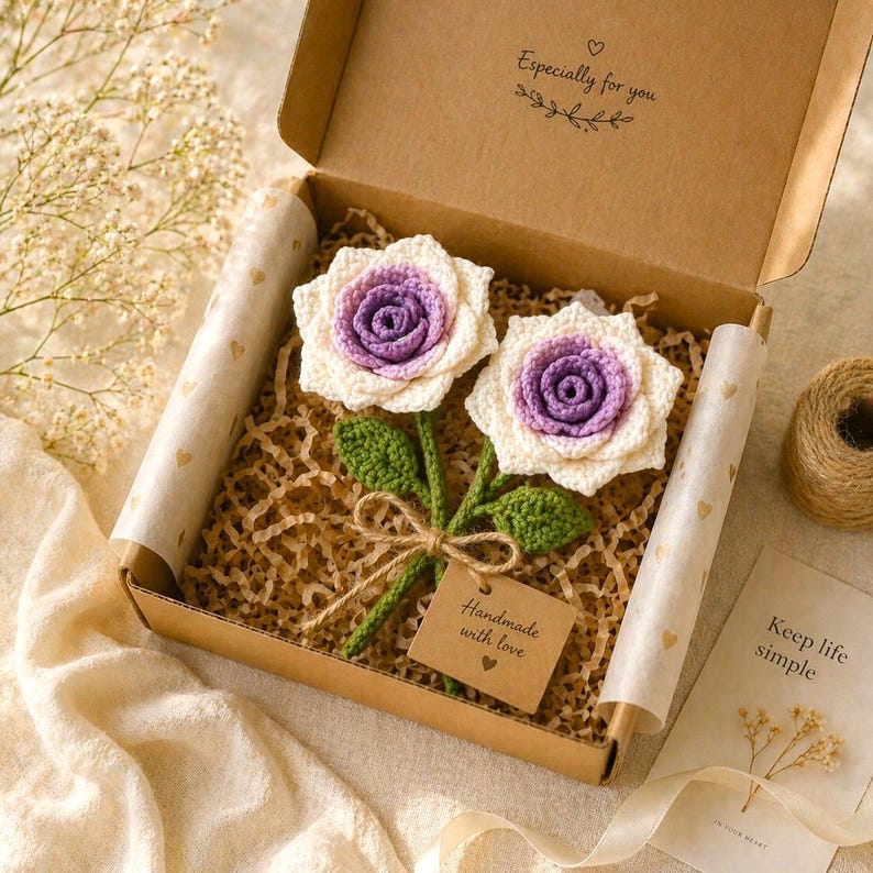 May include: Two handmade crochet roses in a gift box. The roses have white petals with purple centers and green leaves. The box is brown with the text "Especially for you" and a tag that says "Handmade with love".