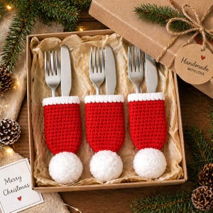 Peut inclure: Un ensemble cadeau de No&euml;l avec trois fourchettes et couteaux, chacun dans un bonnet de P&egrave;re No&euml;l rouge et blanc tricot&eacute;. L'ensemble est pr&eacute;sent&eacute; dans une bo&icirc;te en carton, orn&eacute;e de verdure festive et d'une &eacute;tiquette indiquant "Handmade with Love". Une carte dit "Joyeux No&euml;l".