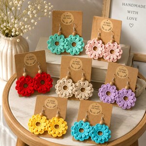 May include: A collection of handmade crochet flower earrings in various colors, including red, yellow, turquoise, pink, cream, and purple. Each pair is displayed on a brown card with the text "EL EMEGI GOZ NURU". The earrings have silver hooks and wooden bead accents.