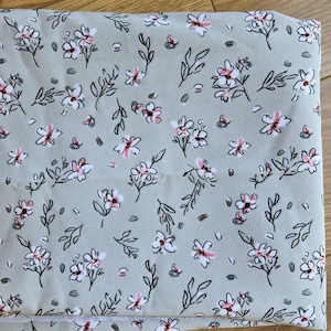 May include: A folded piece of light sage green fabric featuring a repeating pattern of small white flowers with black outlines and soft pink centers, interspersed with delicate black leafy stems and small dark gray dots throughout the design.
