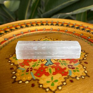 May include: A white selenite stick resting on a wooden tray with a colorful floral design.