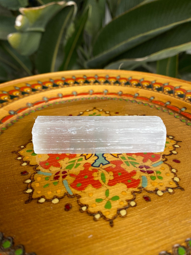 May include: A white selenite stick resting on a wooden tray with a colorful floral design.