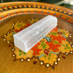 May include: A white selenite crystal stick on a wooden tray with a colorful floral design.