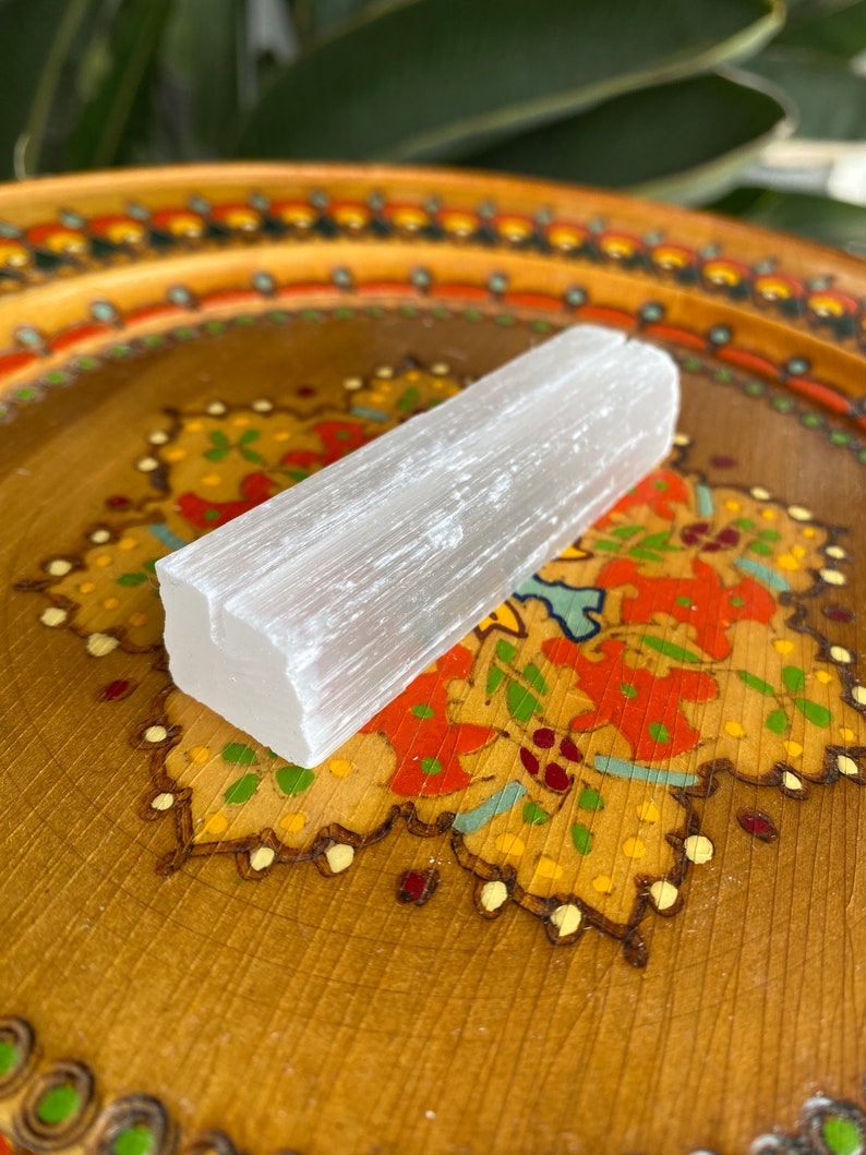 May include: A white selenite crystal stick on a wooden tray with a colorful floral design.