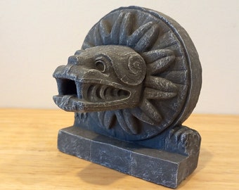 May include: A grey stone sculpture of a mythical creature with a circular design on its back. The sculpture is on a rectangular base.