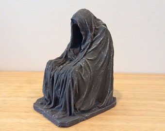 Könnte beinhalten: Eine graue, verhüllte Figuren-Skulptur, die auf einem Sockel sitzt. Die Figur ist in eine lange, fließende Robe mit einer tiefen Kapuze gehüllt.