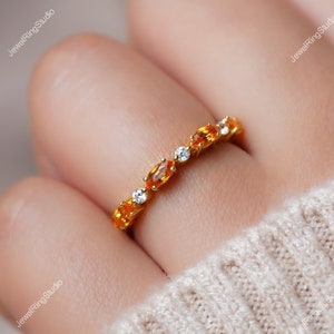 May include: A delicate gold band ring with a row of oval-shaped orange gemstones and smaller round white gemstones.