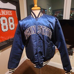 Puede incluir: Una chaqueta bomber de satén azul marino con letras blancas y doradas que dicen "Penn State".