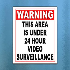 以下が含まれることがあります： 白い背景と赤い縁取りの長方形の看板。 「WARNING」の文字が赤い背景に太字の白い文字で上部にあります。 下には、黒で「THIS AREA IS UNDER 24 HOUR VIDEO SURVEILLANCE」と書かれています。