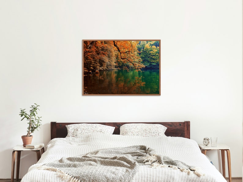 May include: A framed photograph of a lake surrounded by trees with fall foliage. The water is still and reflects the trees and sky. The colors are vibrant and warm, with shades of orange, yellow, green, and blue.
