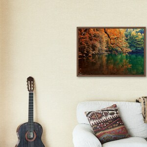 May include: A framed photograph of a lake surrounded by trees with fall foliage. The water is a deep green and the trees are a mix of orange, yellow, and red.