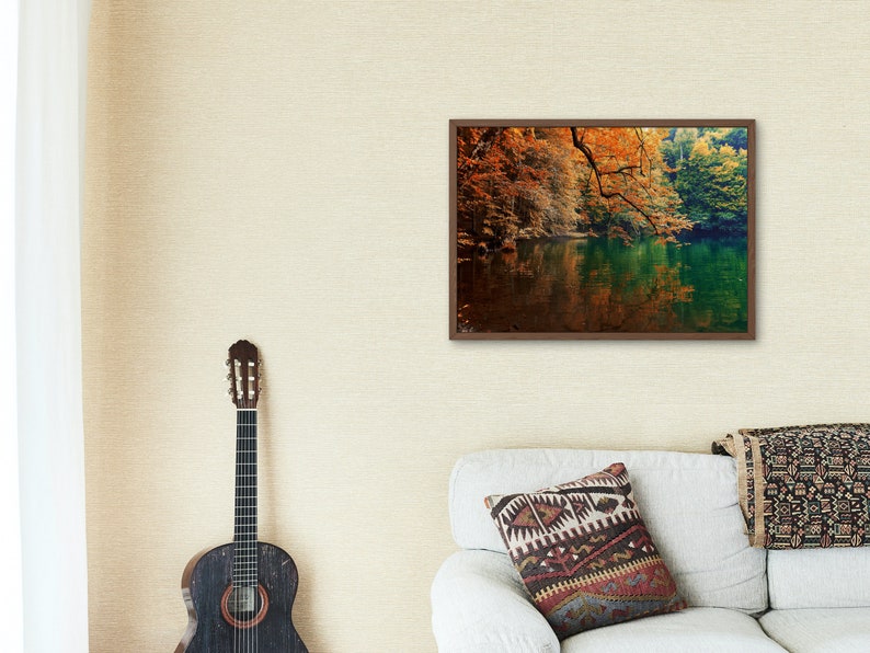 May include: A framed photograph of a lake surrounded by trees with fall foliage. The water is a deep green and the trees are a mix of orange, yellow, and red.