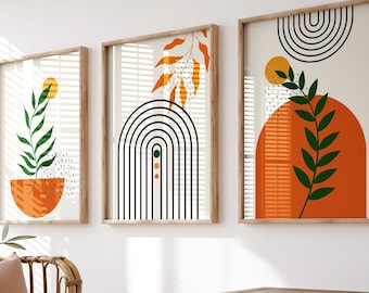 Könnte beinhalten: Drei abstrakte Kunstdrucke mit orangefarbenen, grünen und schwarzen geometrischen Formen und Blattdesigns. Die Drucke sind in Naturholz gerahmt und an einer weißen Wand aufgehängt. Ein Korbstuhl mit einem braunen Kissen und einer weißen Wolldecke steht vor den Drucken. Ein weißer Schrank mit einer Holzplatte steht rechts neben dem Stuhl.