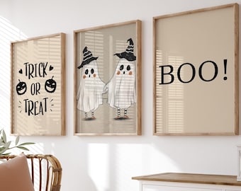 May include: Three framed Halloween-themed prints with white backgrounds. The left print says "Trick or Treat" with a pumpkin on each side of the word "or". The middle print features two ghosts wearing witch hats. The right print says "BOO!" in black text.