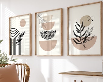 May include: Three framed abstract art prints with a minimalist design featuring geometric shapes, leaves, and dots in black, white, and pink. The prints are hanging on a white wall above a white cabinet with a wooden top.