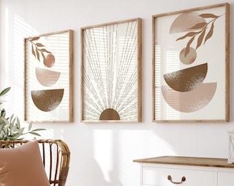 Puede incluir: Un armario blanco con dos cajones y dos puertas, una cesta de mimbre, una silla de mimbre marrón con un cojín rosa y una manta blanca, y tres impresiones enmarcadas con diseños geométricos abstractos en tonos marrones y rosas.