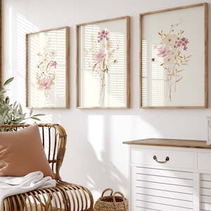May include: A light wood cabinet with two white doors and a wood top. The cabinet has a white, slatted design on the doors. A wicker basket sits on the floor in front of the cabinet. A brown wicker chair with a tan cushion sits in front of the cabinet. Three framed floral prints hang on the wall behind the cabinet.