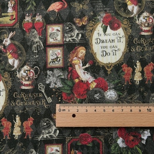 Könnte beinhalten: Ein schwarzer Stoff mit einem Alice im Wunderland-Druck, der ein Mädchen, einen Hasen, einen Flamingo und Teekannen zeigt, sowie den Text "If you can dream it, you can do it." Ein Holzlineal zeigt eine Skala von 10 cm am unteren Rand.