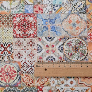Può includere: Un tessuto patchwork con una varietà di piastrelle quadrate e rettangolari con motivi intricati. Le piastrelle mostrano un mix di colori, tra cui rosso, blu, arancione e bianco, con disegni floreali e geometrici. Un righello di legno è posto sul tessuto.