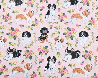 May include: Pink fabric featuring a repeating pattern of various dog breeds, including Cavalier King Charles Spaniels, interspersed with floral bouquets in shades of pink, yellow, and green. The dogs are depicted in various poses.