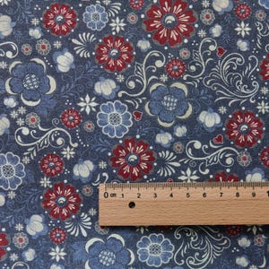Könnte beinhalten: Nahaufnahme eines Stoffes mit floralem Muster. Das Design zeigt rote, blaue und weiße Blumen, zusammen mit weißen Wirbelranken und kleinen Herzen, vor einem dunkelblauen Hintergrund. Ein Holzlineal liegt auf dem Stoff.