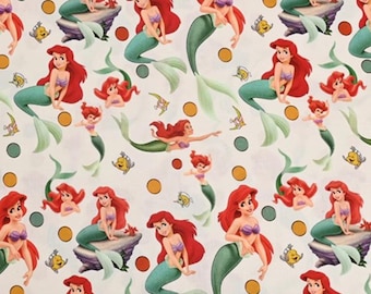 May include: White fabric featuring a repeating pattern of a mermaid with red hair, a purple seashell bra, and a teal tail. The mermaid is depicted in various poses, with yellow and orange circles and small yellow fish scattered throughout.
