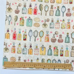 May include: A white fabric with a repeating pattern of vintage perfume bottles and hand mirrors. The bottles are in various colors, including blue, green, pink, and yellow. The mirrors are gold and have ornate handles.