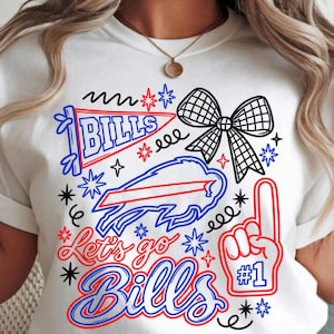 Może przedstawiać: Biały t-shirt z grafiką zawierającą napis "BILLS", "Let's go Bills" oraz "#1". Nadruk przedstawia niebieski proporczyk, czarno-białą kokardę w kratkę, zarys niebieskiego bizona oraz czerwoną piankową dłoń z niebieskimi akcentami.