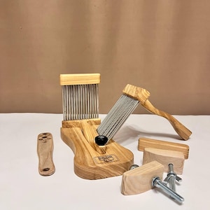May include: A collection of wooden fiber tools, including a large comb, a smaller comb, a handle, and clamps. The tools are made of light-colored wood with metal tines and hardware. The tools are designed for fiber arts.