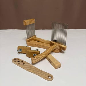 May include: A collection of wooden fiber art tools, including a comb, a paddle, and various hardware pieces. The tools are made of light-colored wood and feature metal tines and screws. The items are arranged on a white surface.