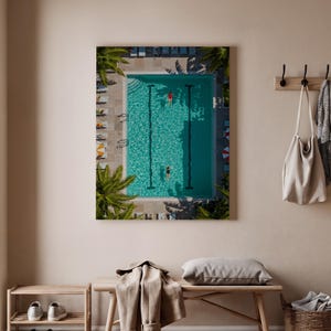 Könnte beinhalten: Draufsicht auf ein rechteckiges Schwimmbecken mit zwei Schwimmern. Das Becken ist mit türkisfarbenem Wasser gefüllt und von Palmen und Liegestühlen umgeben. Ein Schwimmer trägt einen roten Badeanzug, der andere einen schwarzen.