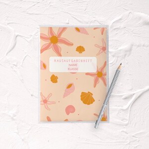 Könnte beinhalten: Ein rosa-oranges Hausaufgabenheft mit einem Muschel- und Seesternmuster. Der Umschlag hat ein Etikett mit der Aufschrift "Hausaufgabenheft" und Platz für "Name" und "Klasse".