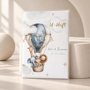 Könnte beinhalten: Eine transparente Schutzhülle für ein U-Heft mit einer Aquarellillustration eines blauen Heißluftballons, der eine Giraffe, einen Elefanten, einen Bären und einen Löwen trägt, sowie dem Text U-Heft, Vor & Zuname und XX-XX-20XX.