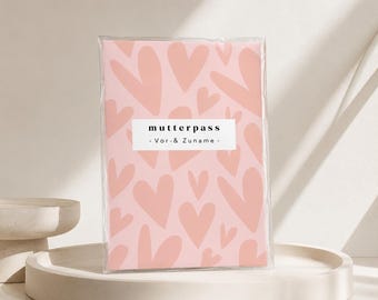 May include: A rectangular protective cover for a document featuring a light pink background with a pattern of darker pink hearts. A white horizontal label in the center displays the black text "mutterpass" and "- Vor- & Zuname -."