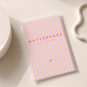 Könnte beinhalten: Ein rechteckiges Heft in einer transparenten Kunststoffhülle mit vertikalem Streifenmuster in Helllila und zartem Orange. Der Text MUTTERPASS - VOR- & ZUNAME - ist in Pink gedruckt, ergänzt durch ein kleines pinkes Herzsymbol darunter.